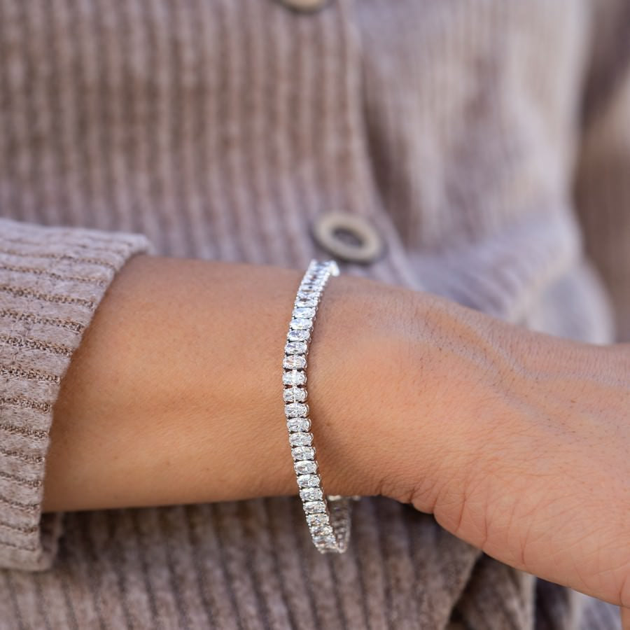 10ct oval tennis bracelet stacked with yellow gold bangles on wrist