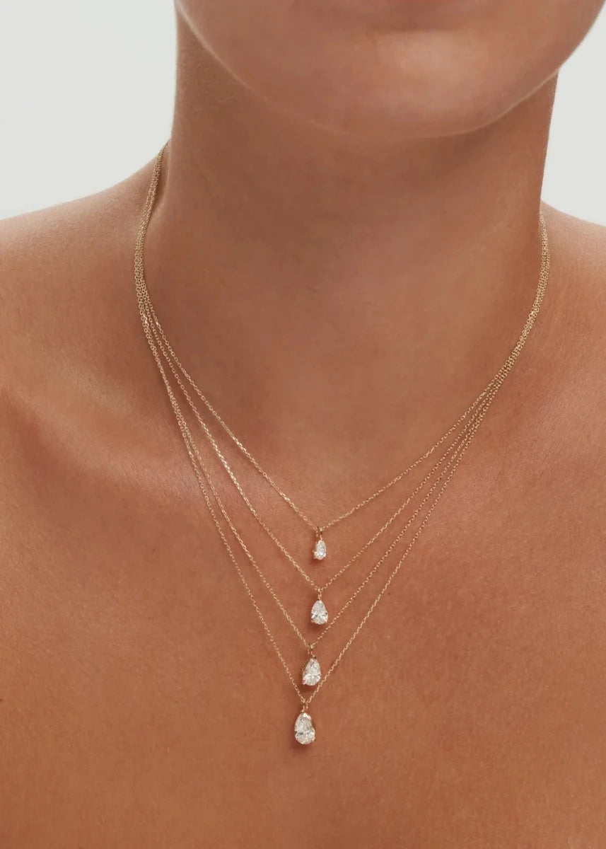 Close-up of a person wearing a delicate gold necklace with three small pendant drops on a neutral background.