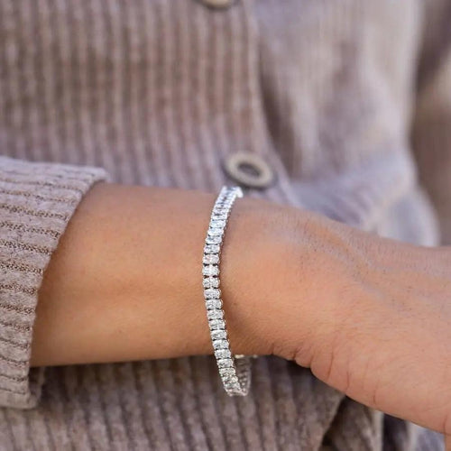 10ct oval tennis bracelet stacked with yellow gold bangles on wrist